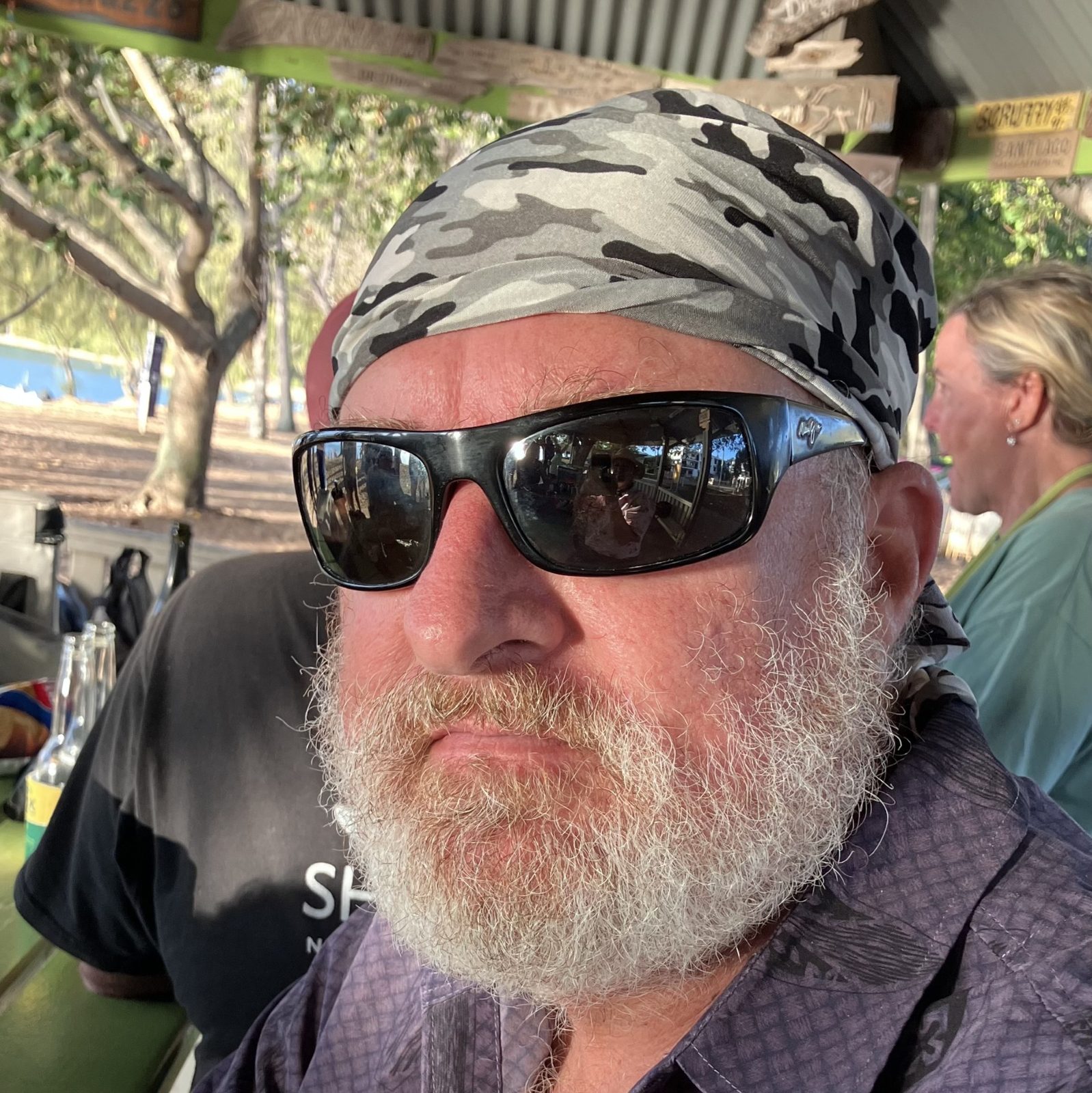 Dave at a waterfront bar in sunglasses, a grey camo neck sock worn as a beanie
