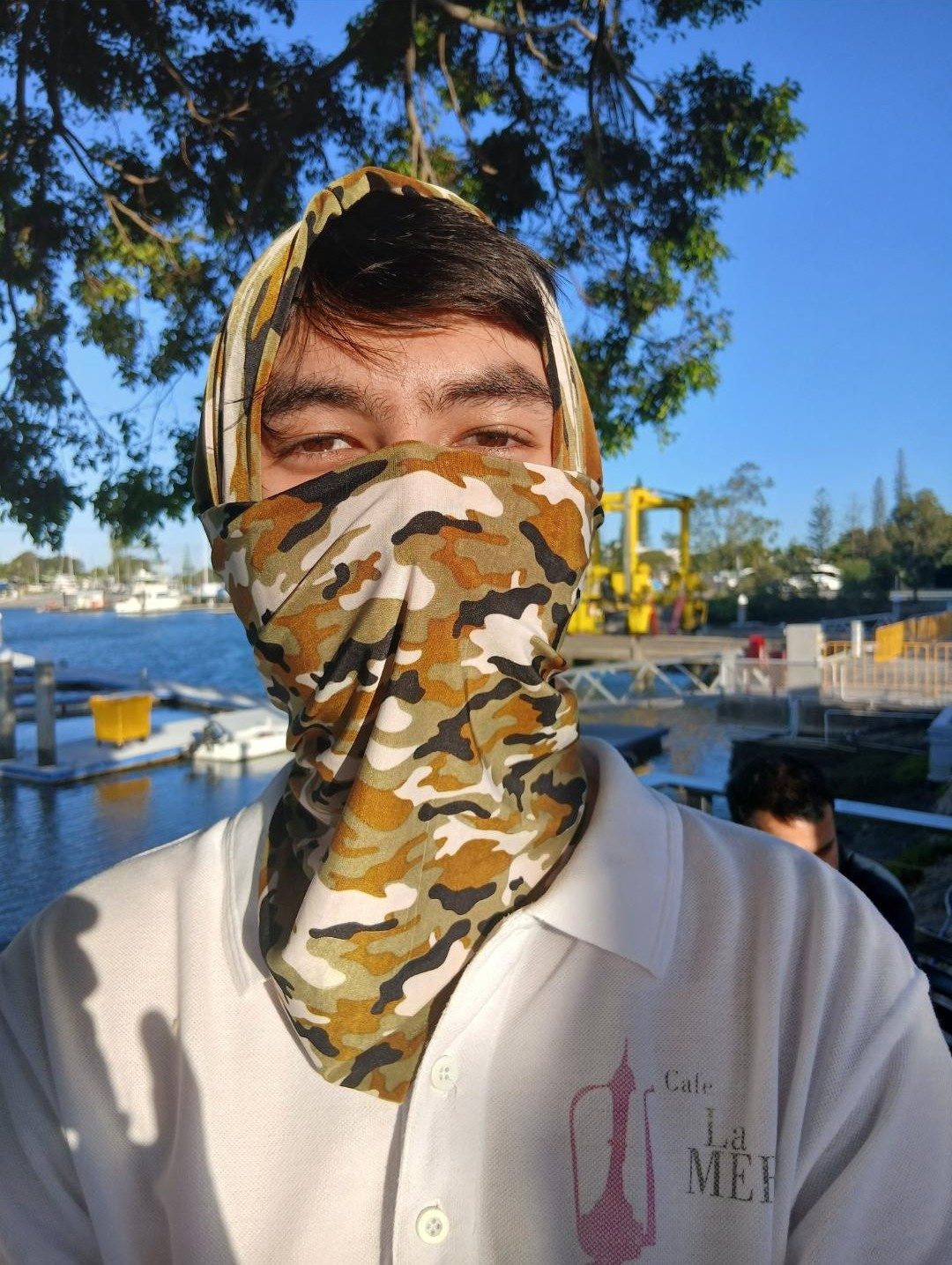 A young man at the marina with a camo neck sock over his face and a second one twisted around his head